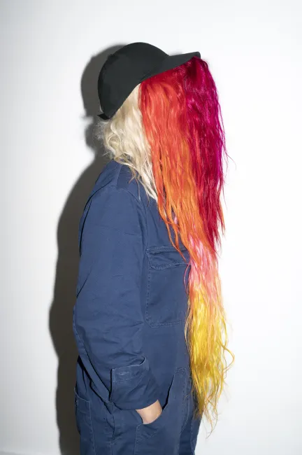Portrait photo de l'artiste Julie Monot avec une casquette et cheveux colorés couvrant son visage
